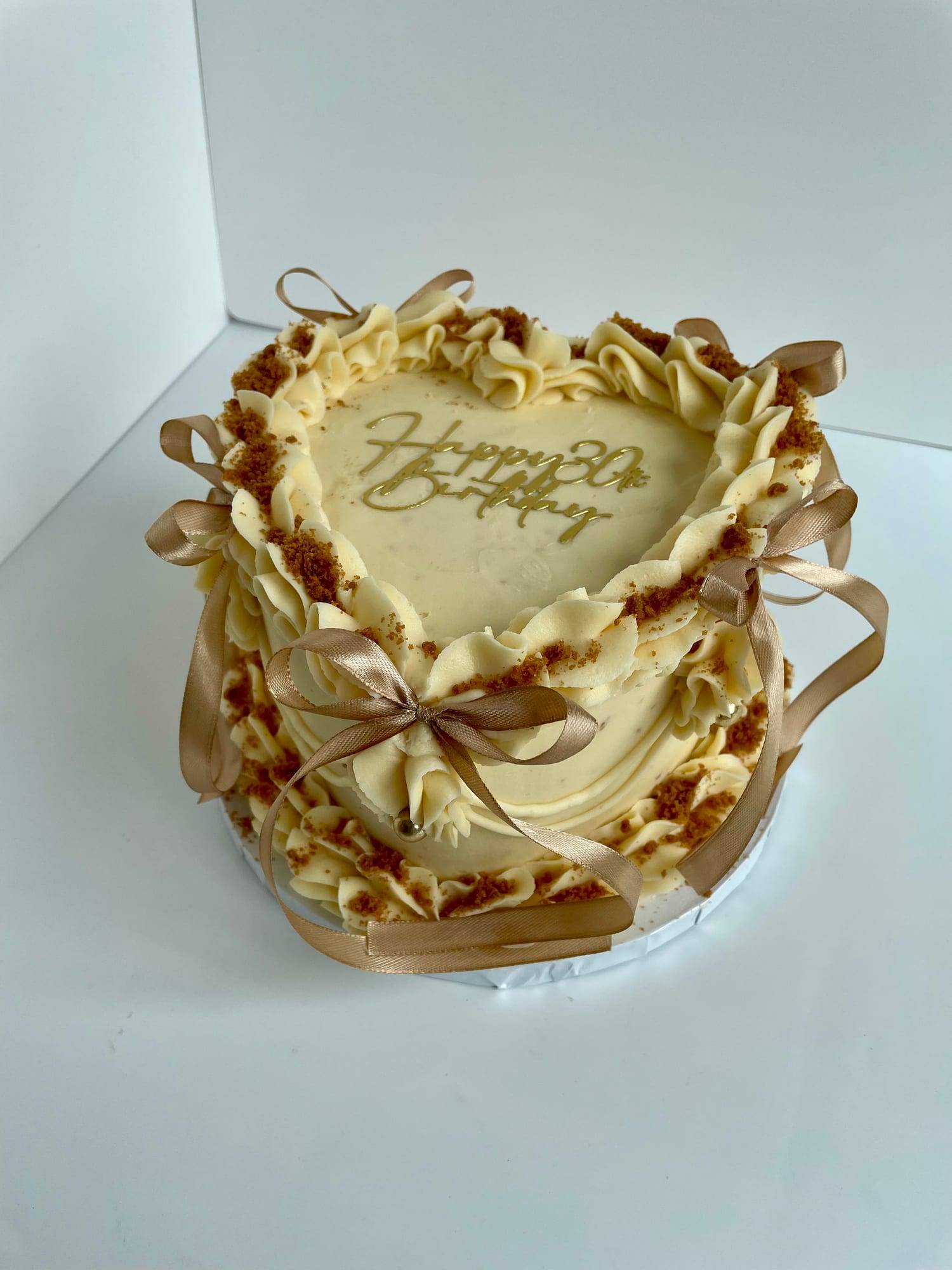 Heart-shaped 30th birthday cake with ivory ruffled buttercream, biscuit crumb edging and gold ribbon bows