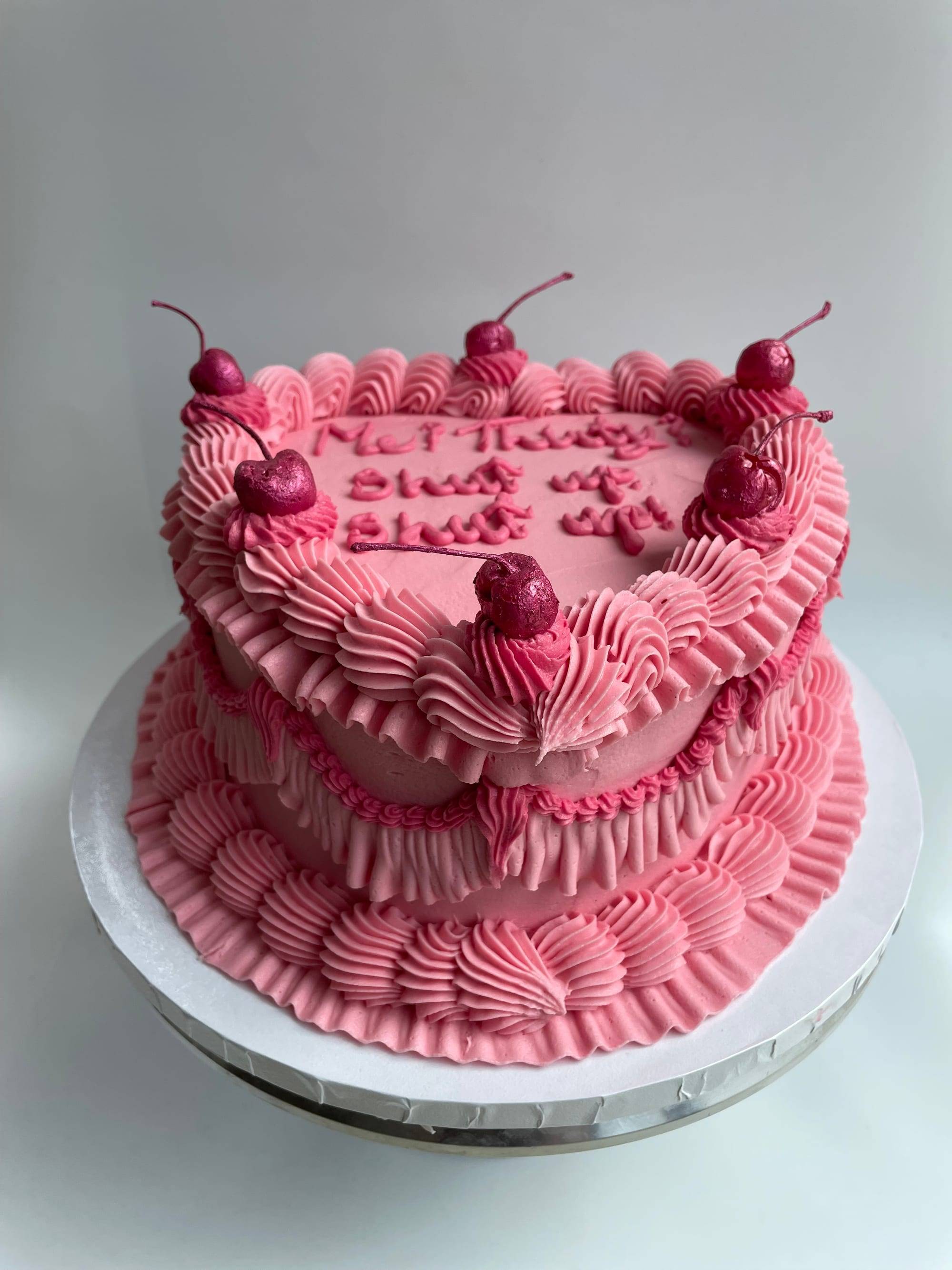 Two-tier heart-shaped 30th birthday cake in hot pink shell-piped buttercream with glacé cherries and a playful iced message