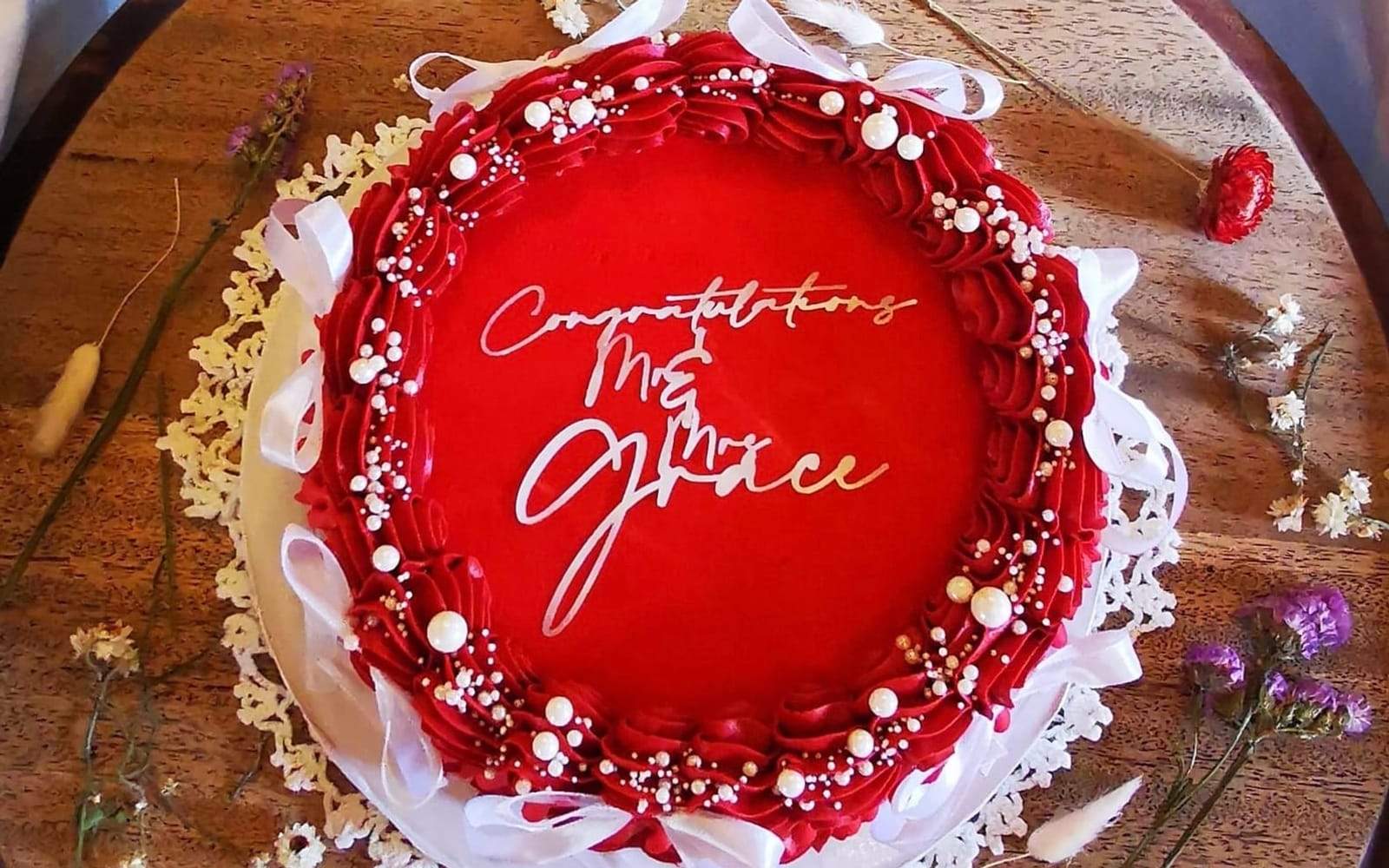 Round wedding cake with a red buttercream shell border, pearl beading and a gold Congratulations message